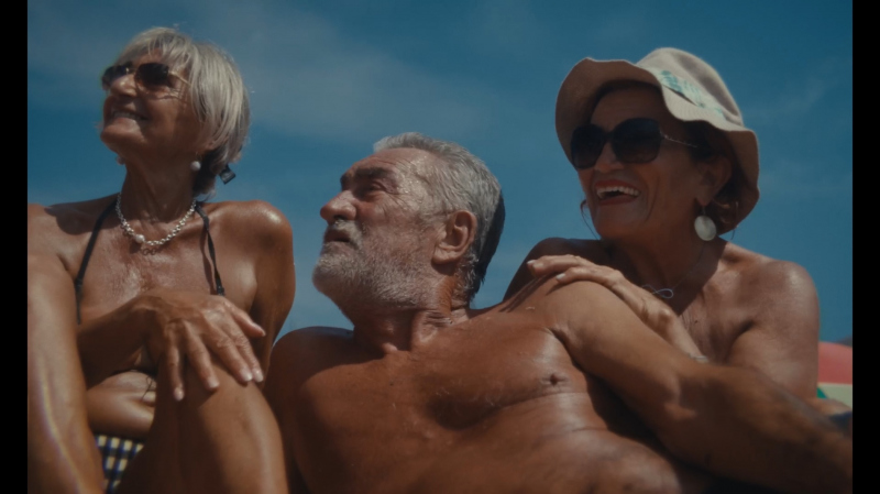 Trzy starsze osoby siedzą razem na plaży w pełnym słońcu.